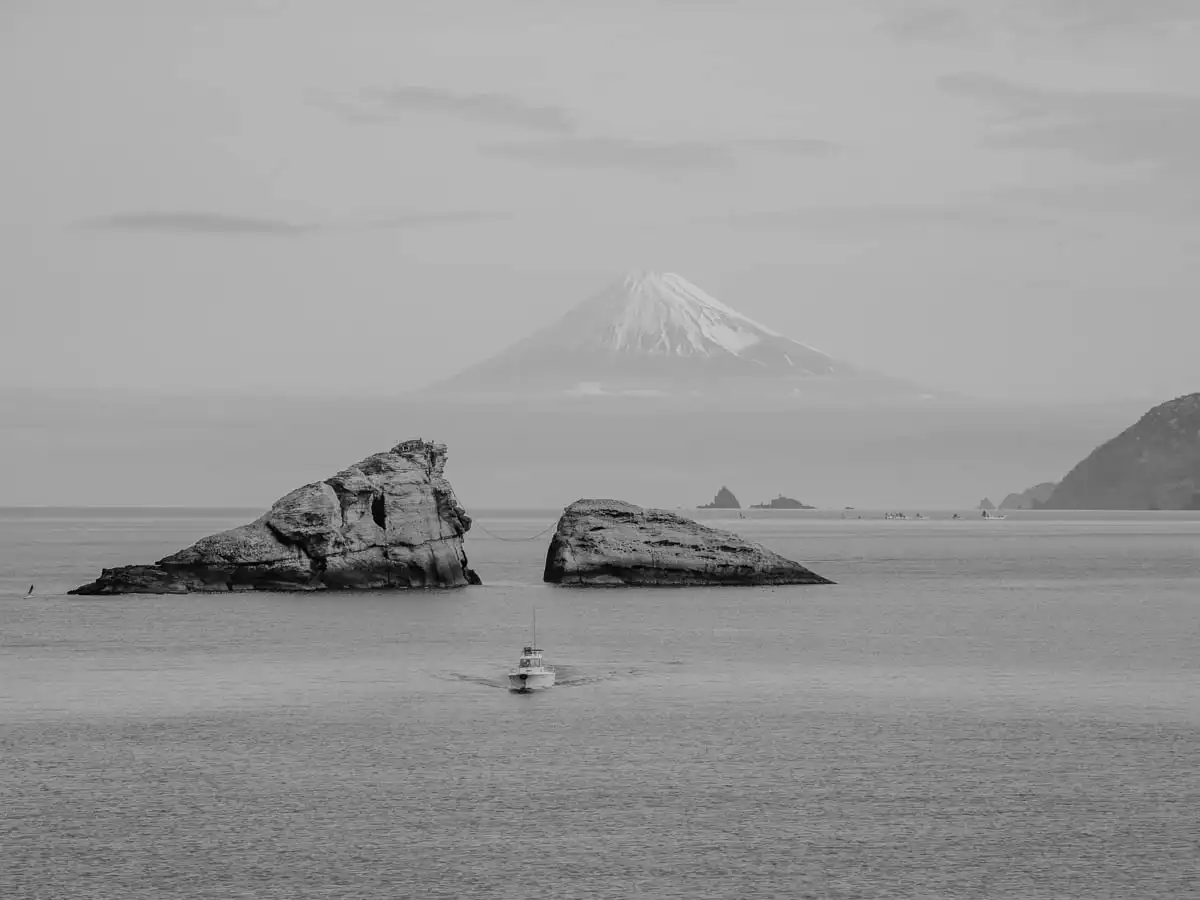 two small island rocks aligning with mount fuji and a boat passing by. One of the best things to do in izu peninsula