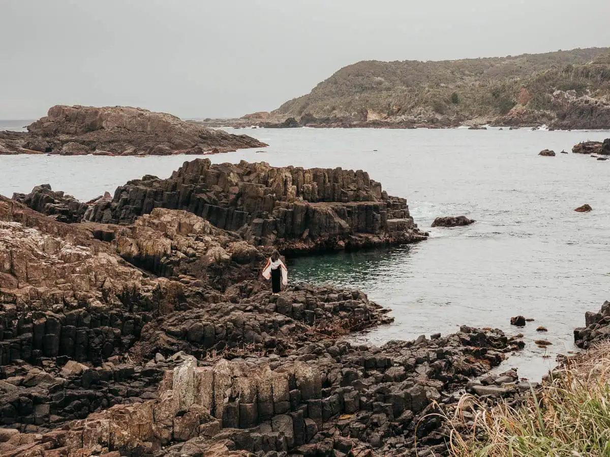 woman standing on the rocky outcrop with black volcanic rock