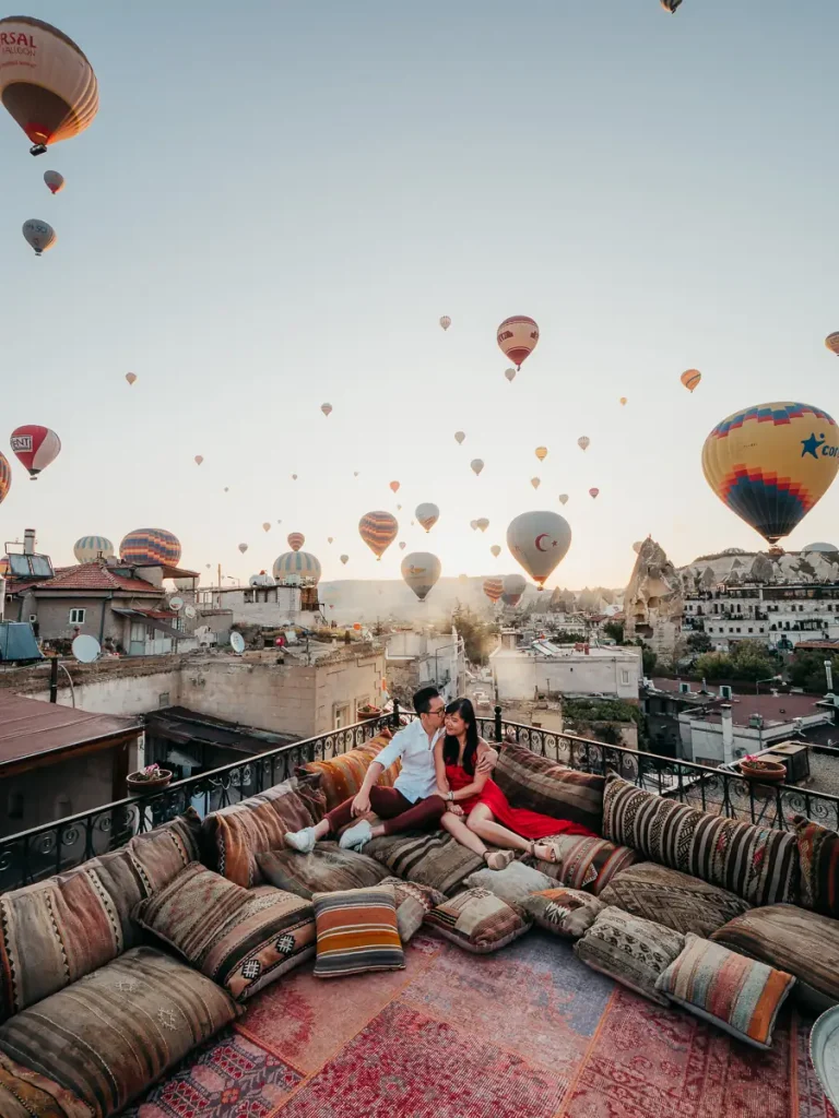 Man and woman sitting on turkish carpets in front of balcony with hot air balloons