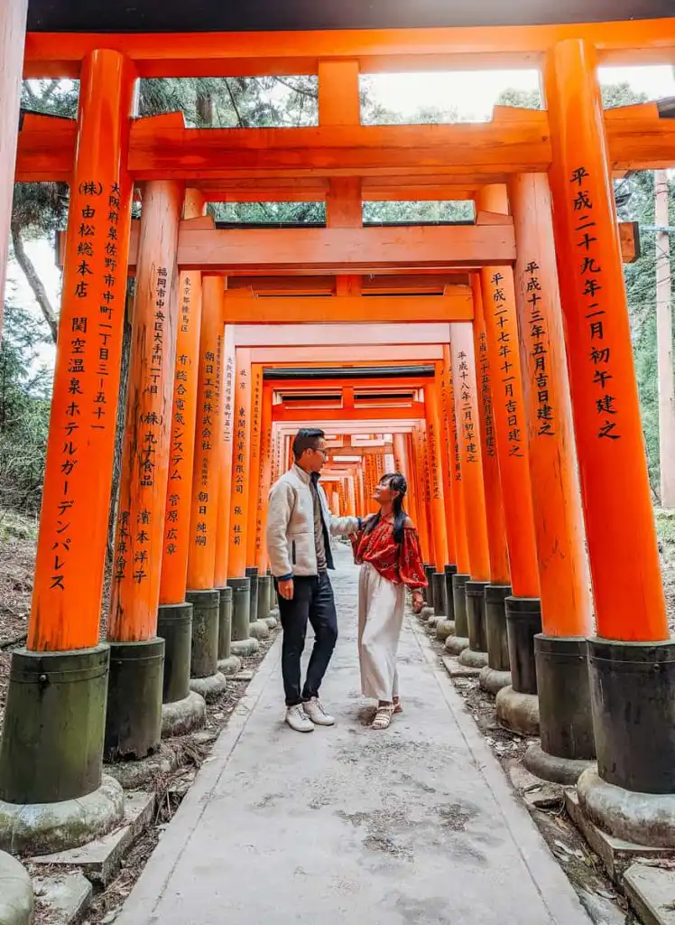 Man and woman standing at the tori gates of Fushimi Inarii, one of our favourite activities during our 2 days kyoto itinerary