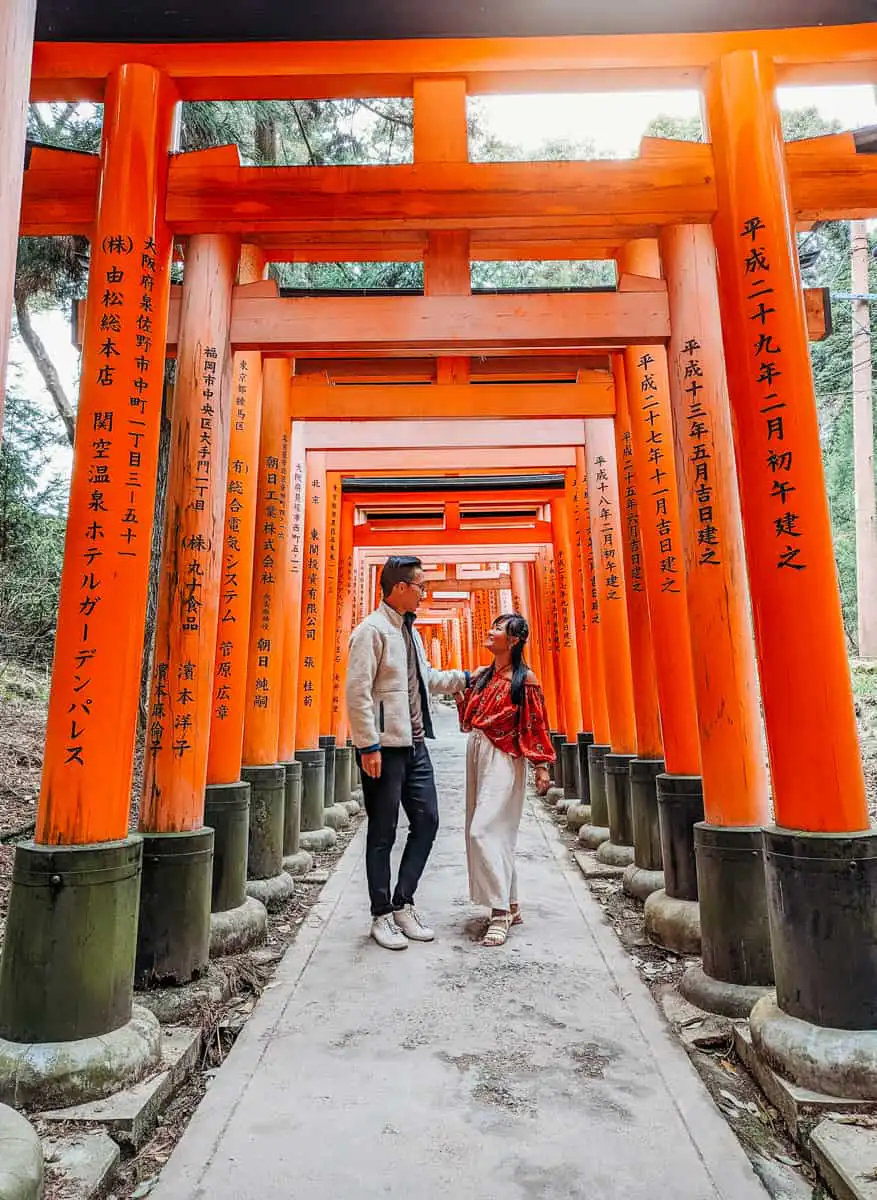 Man and woman standing at the tori gates of Fushimi Inarii, one of our favourite activities during our 2 days kyoto itinerary