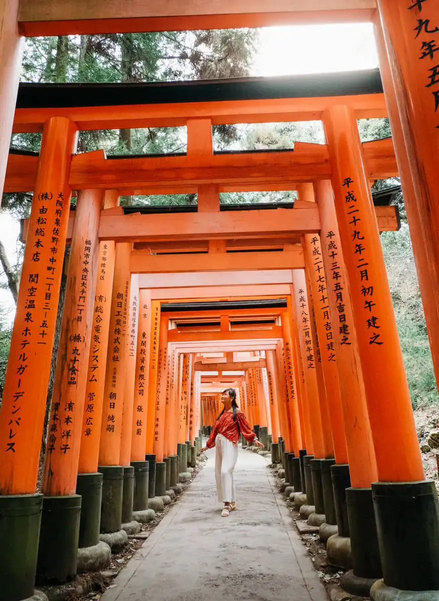 Woman standing in rows of tori gates at Fushimi Inarii
