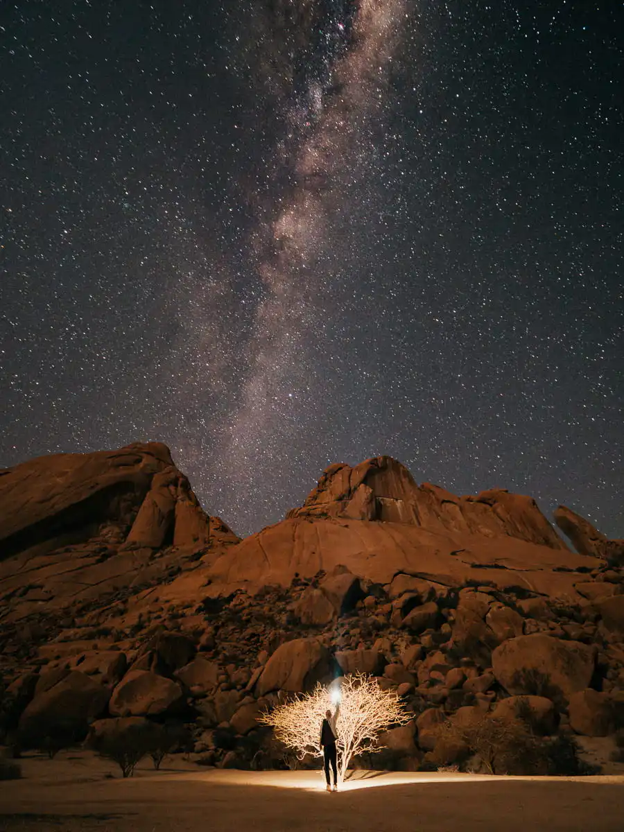 Milky way night sky in Spitzkoppe, man holding light to the tree
