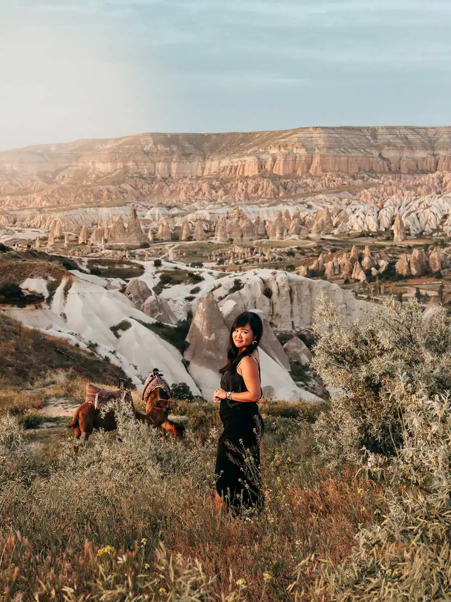 Woman standing in front of camels in Red valley Cappadocia