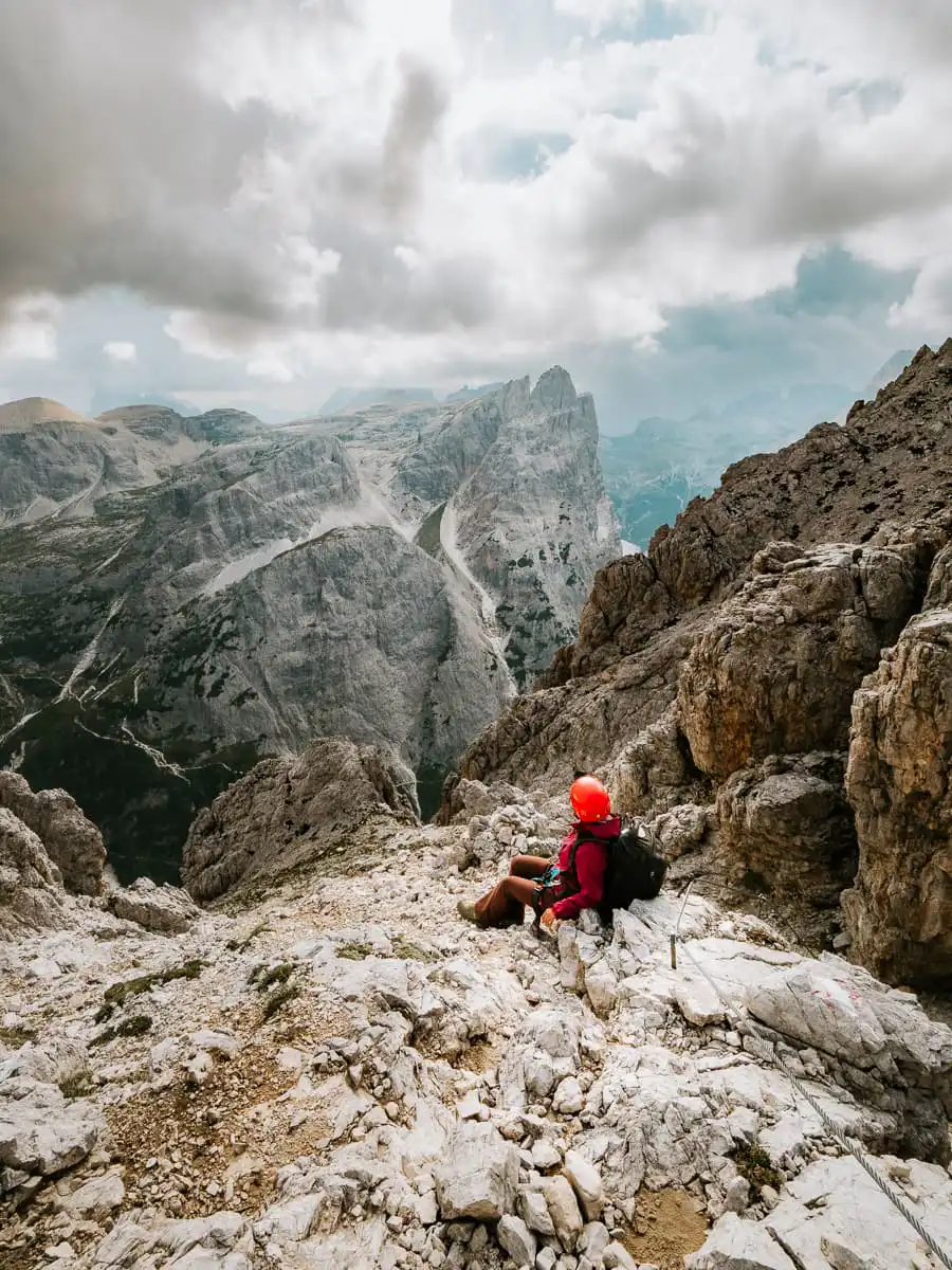 Woman sitting with red helmet high above the mountains in the dolomites