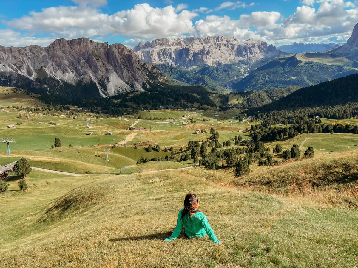 Woman sitting in the grass field overlooking Seceda Valley