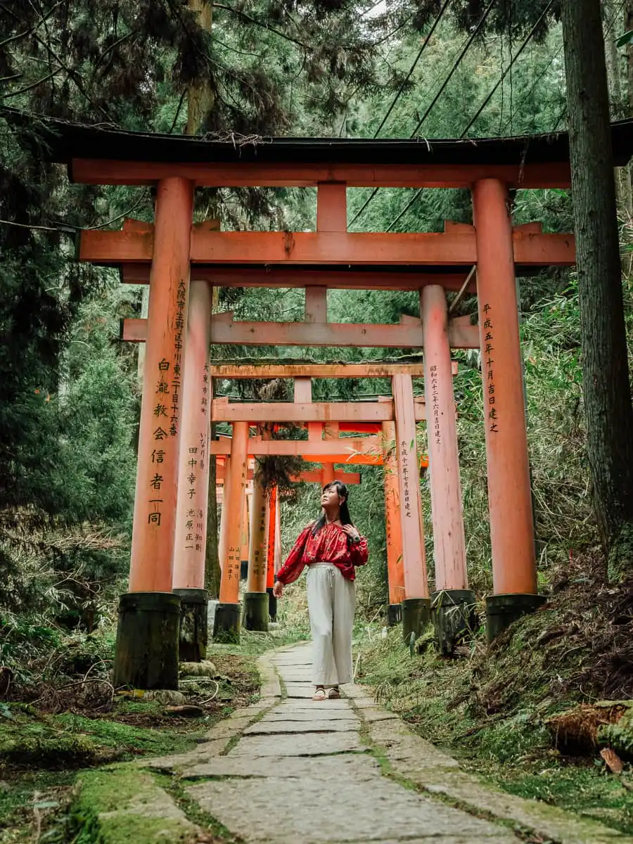 Fushimi Inari Gates covered in moss, woman standing there, one of best day trip from Osaka