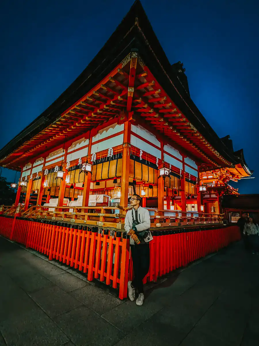 man standing next to red temple at fushimi inari
