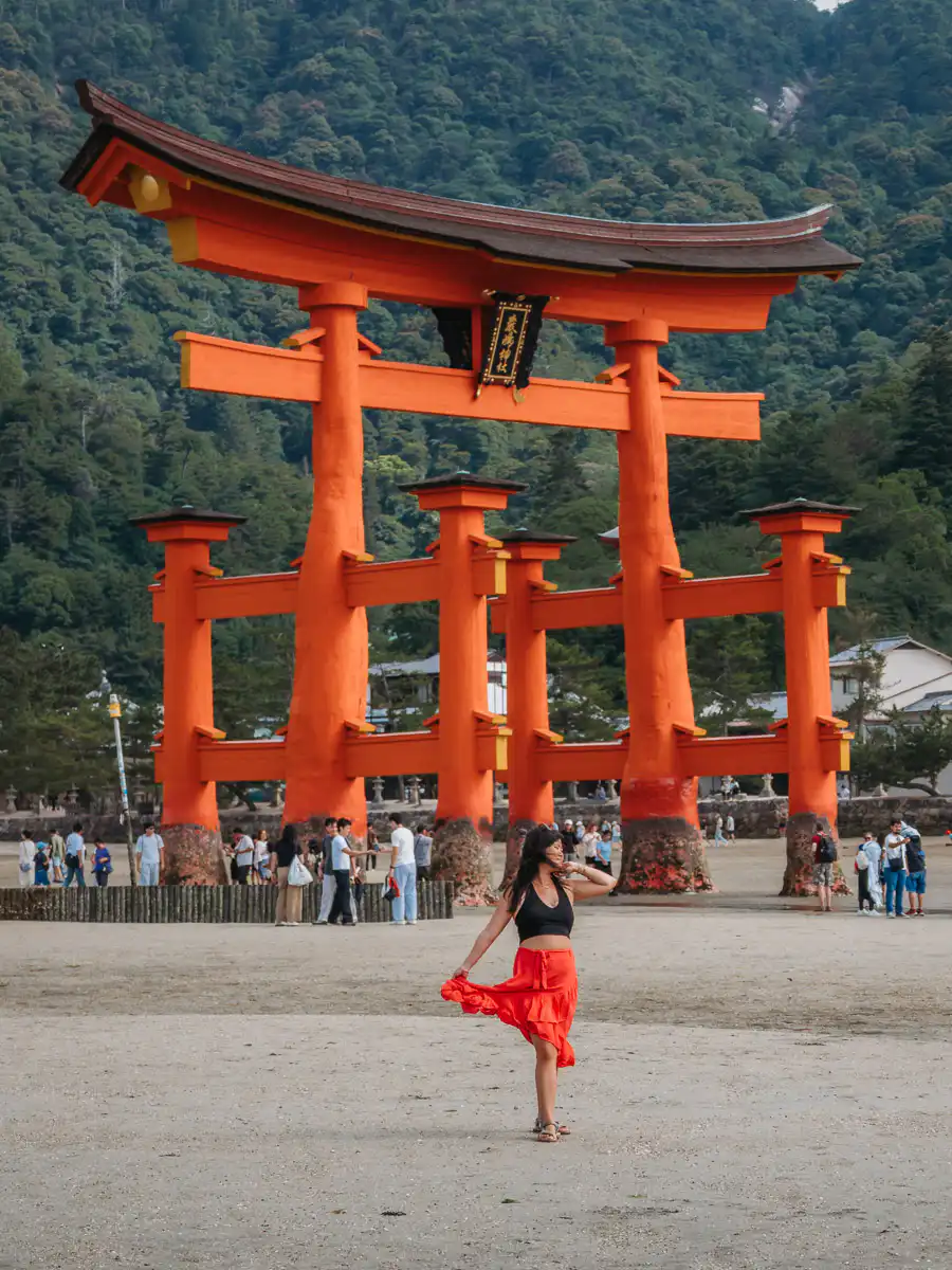woman standing in front of red tori gate on miyajima